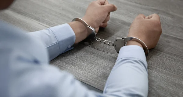 selective-focus-shot-male-hands-handcuffs-wooden-table